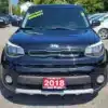 A black 2018 Kia Soul EX is parked front-facing in a car lot, featuring a Why Not Warranty? sticker on the windshield. The red license plate displays Boss Auto and a contact number, with other vehicles in the background.