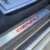 Close-up of a 2016 GMC Acadia Denali AWD door sill features a metallic plate with Denali in bold red letters, with an AWD car mat outline visible in the dim light.