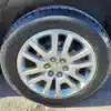 Close-up of a silver alloy wheel with a geometric spoke design from a 2016 GMC Acadia Denali AWD. The black tire, in good condition, shows visible tread and sidewall details, ready for tackling terrains in style on a paved surface.