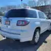 A white 2016 GMC Acadia Denali AWD SUV sits outdoors on a sunny day, showcasing its rear and tinted windows with a Loaded sign visible. Trees and a building form the backdrop.