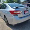 A 2018 Subaru Impreza Sport with Tech package, featuring a Loaded dealership plate, is parked outdoors in a lot. The car glistens under the clear blue sky, surrounded by other vehicles and trees.