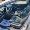 Interior view of a 2018 Subaru Impreza Sport w/ Tech pkg, featuring black leather seats, sport steering wheel, and high-tech dashboard. Sunlight streams in through the open door onto a paper mat with footprints on the drivers side floor.