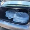 The open trunk of a 2018 Subaru Impreza Sport w/ Tech pkg in silver holds two tires in white plastic bags. The spacious trunk is empty aside from the tires, and the car is parked on a sunlit asphalt surface.