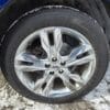 Close-up of a five-spoke alloy wheel with a Goodyear Eagle RSA tire on a blue 2013 Ford Edge SEL V6, resting in the snow. Mud accents the tire tread.