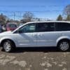 A 2017 Dodge Grand Caravan SE in white is parked in a lot on a sunny day, surrounded by other vehicles and trees, under a clear blue sky.