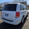 A 2017 Dodge Grand Caravan SE sits outside on a sunny day with snow on the ground and bare trees in the background, featuring a blue dealership plate that reads LIKE NEW.