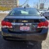 A black Chevrolet car is parked outdoors on a sunny day. The license plate holder reads Certified with contact information for Boss Auto. Several other vehicles and a building are visible in the background.