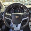 Close-up view of a Chevrolet steering wheel in a car. The dashboard displays speedometer, tachometer, and digital screen. The infotainment system is partially visible on the right, with daylight coming through the windows.