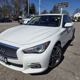 A white 2015 Infiniti Q50 AWD is parked in a car lot, featuring a yellow certified sign on the windshield. In the background, other vehicles and a Boss Auto sign with contact info are visible against the building backdrop.