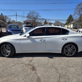 A pristine white 2015 Infiniti Q50 AWD sedan is parked on a paved lot, set against a clear sky with a backdrop of trees and houses.